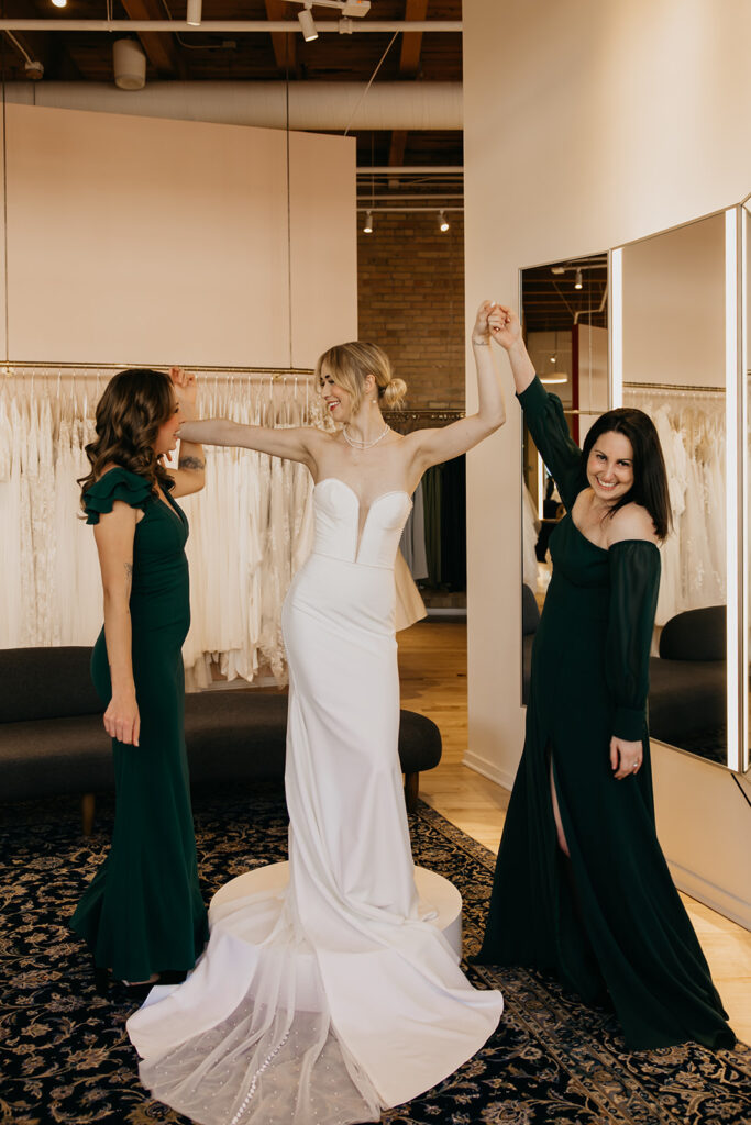 Bride in a modern mermaid gown shares a joyful moment with bridesmaids in emerald gowns at Vow’d Weddings Minneapolis.