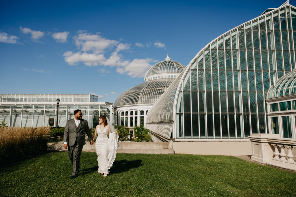 Bride and groom walking outside Como Park Conservatory with blue sky backdrop.