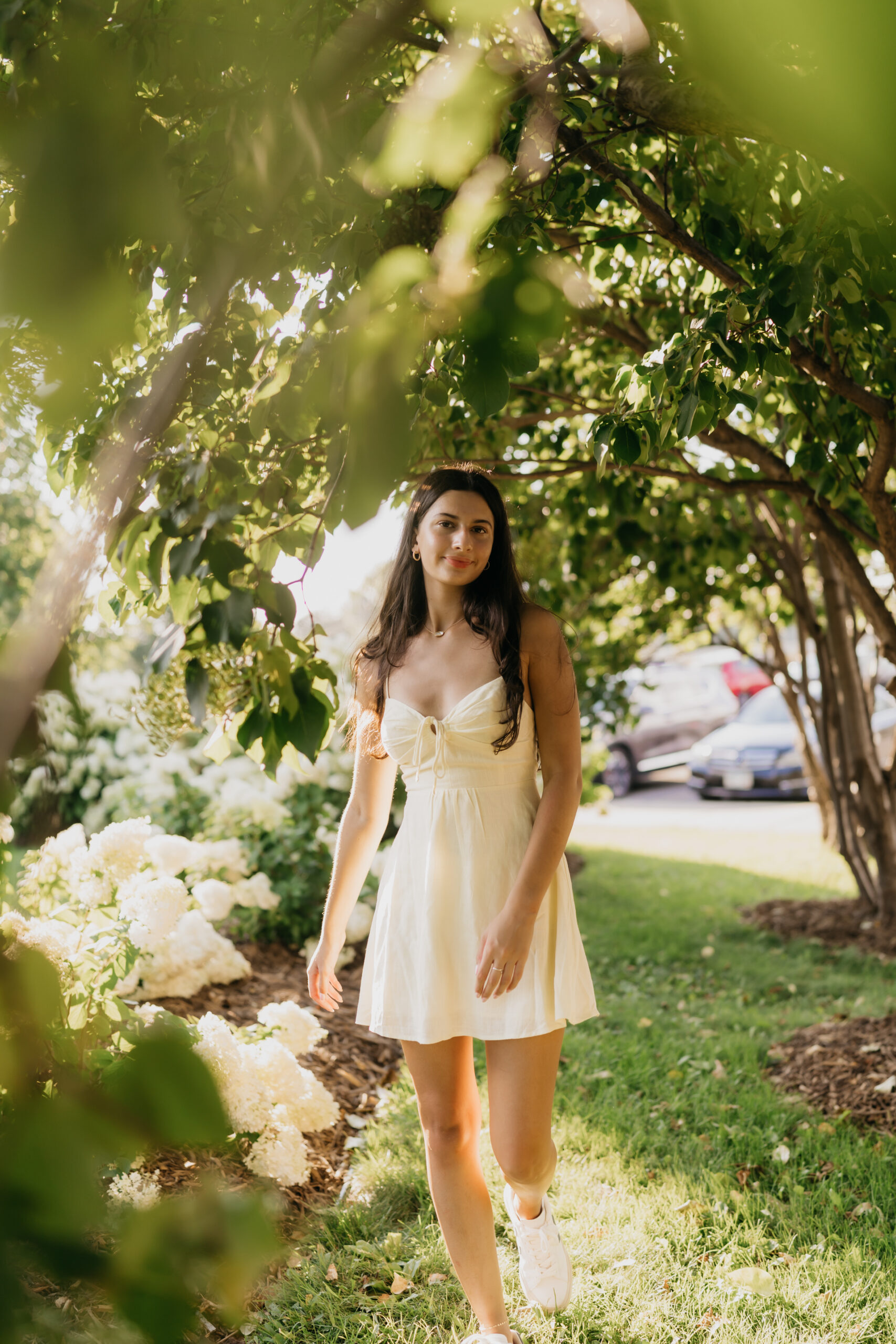 Senior girl walking through a garden in St. Paul, wearing a white dress during her professional senior photo session with Mycah Bain Photography.