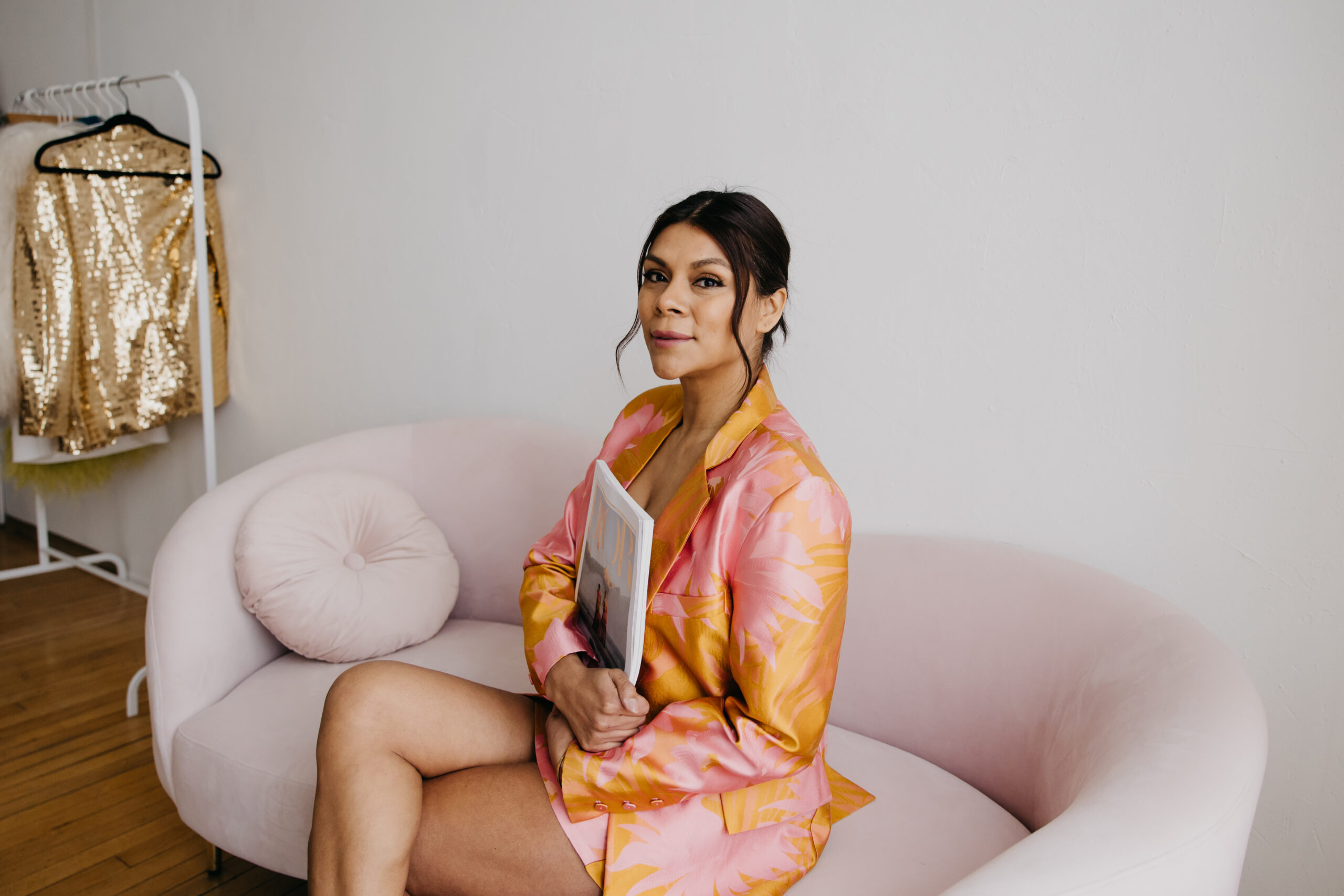 Brenda Iris, founder of Mindful Styling, sits on a blush pink couch wearing a vibrant pink and orange patterned suit during a brand photoshoot in Minneapolis by Mycah Bain Photography.