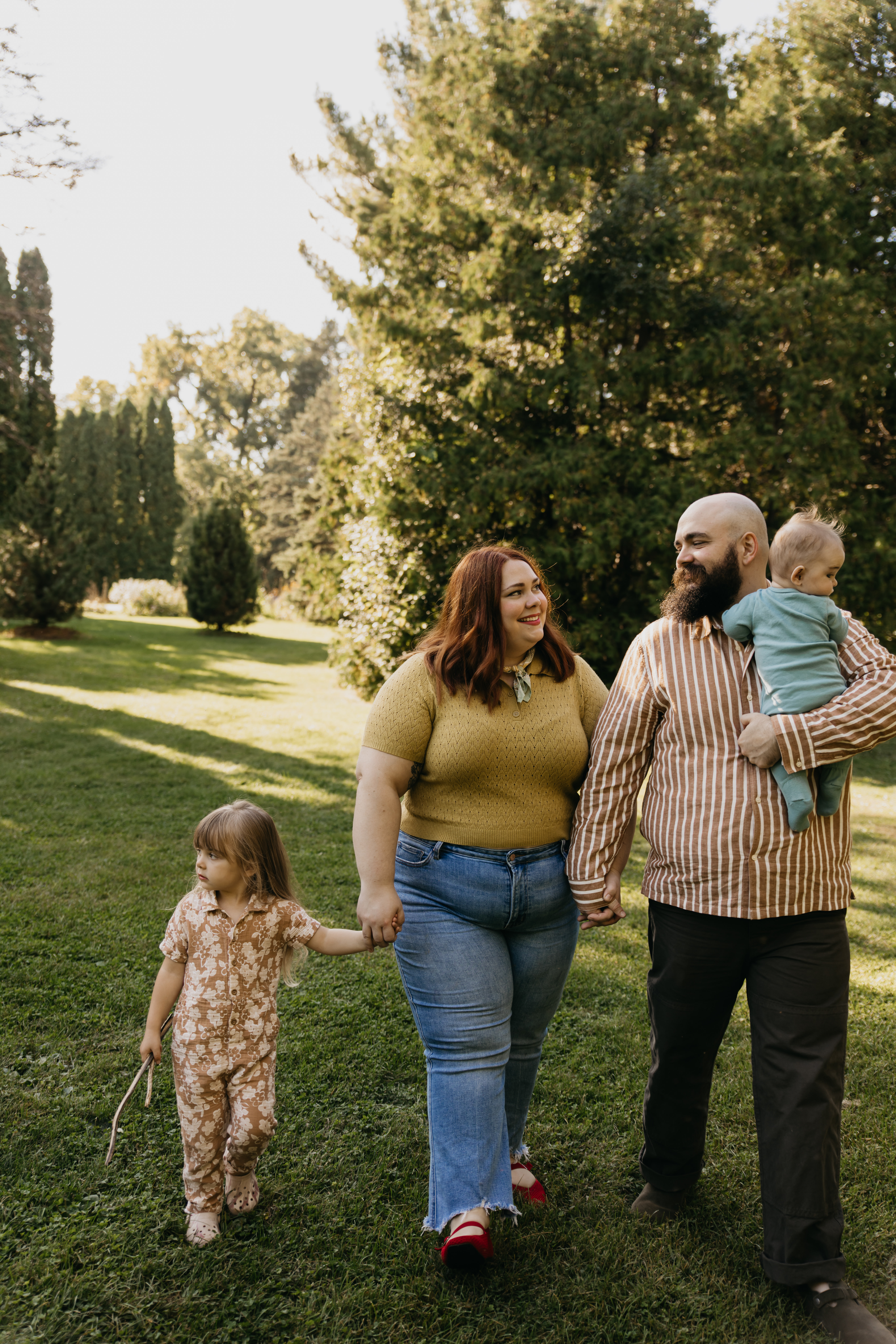 A family of four walking hand-in-hand through the sunlit gardens at Arneson Acres Park in Edina, photographed by Mycah Bain Photography.