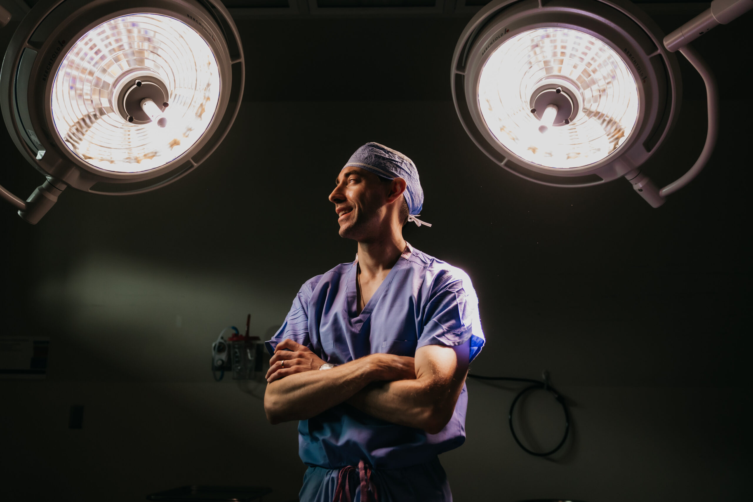 Dr. Matthew Braza stands confidently under surgical lights in an operating room, captured by Minneapolis brand photographer Mycah Bain during a cinematic medical brand photoshoot.