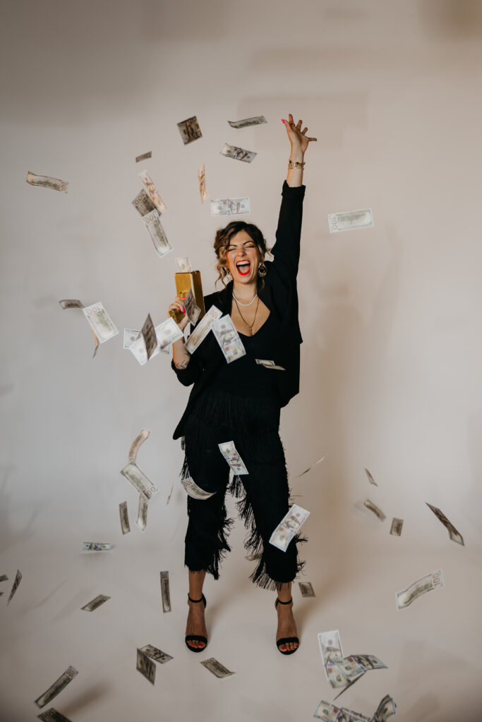 High-energy moment of Dr. Lauryn throwing money in the air, dressed in a black outfit, captured by Minneapolis Luxury Brand Photographer Mycah Bain.