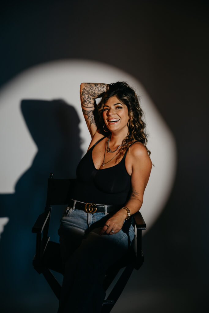 Dramatic studio portrait of Dr. Lauryn in black attire sitting in a director’s chair under a spotlight for her editorial brand session.