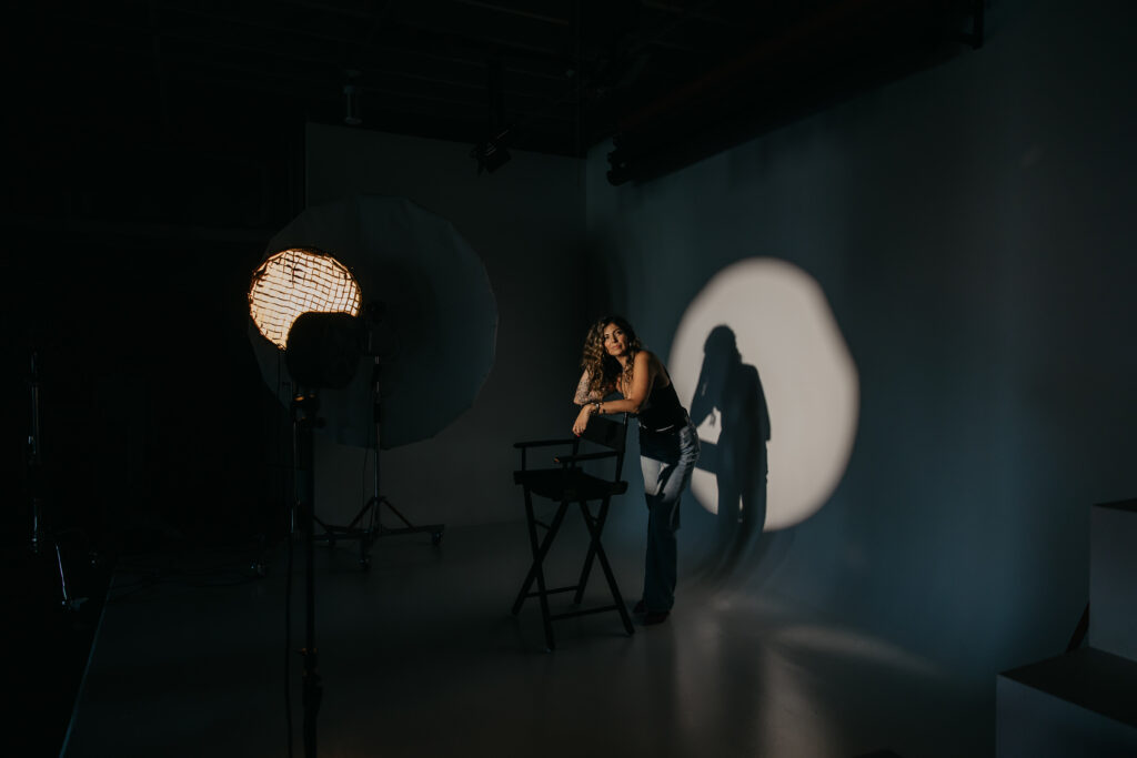 Dramatic studio portrait of Dr. Lauryn in black attire sitting in a director’s chair under a spotlight for her editorial brand session.