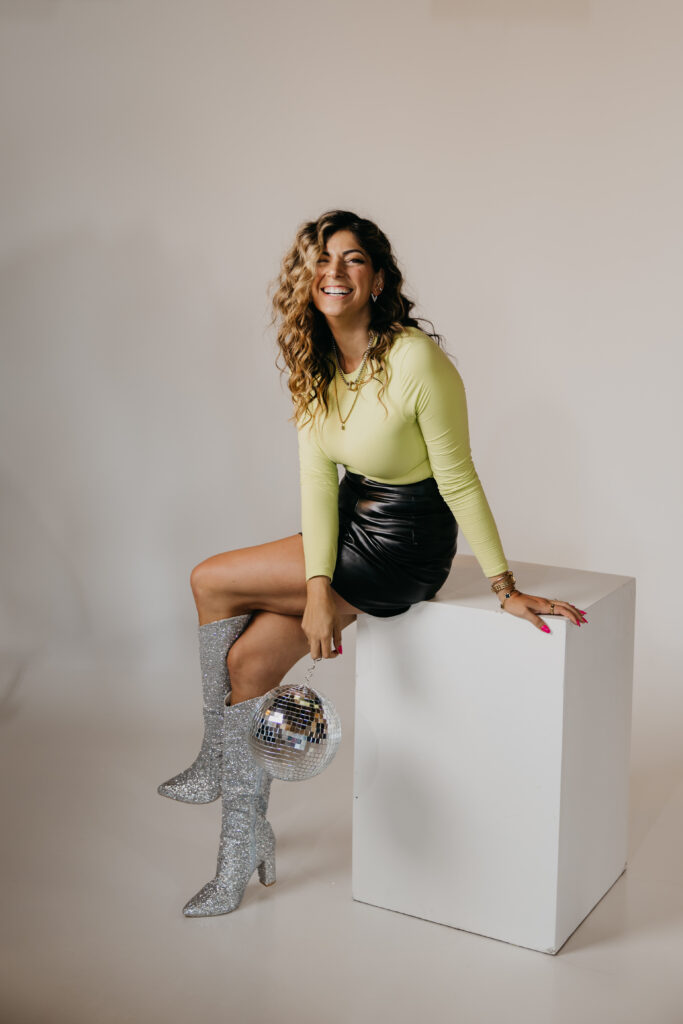 Playful image of Dr. Lauryn lying on the floor with glitter boots and microphone under an “On Air” sign during her brand photoshoot.