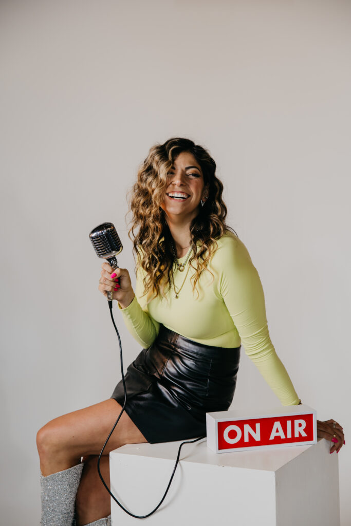 Playful image of Dr. Lauryn lying on the floor with glitter boots and microphone under an “On Air” sign during her brand photoshoot.