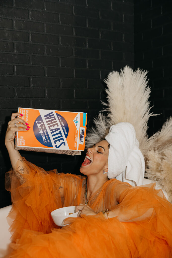 Playful brand photo of Dr. Lauryn wearing an orange robe and towel on her head, eating cereal from a Wheaties box in a Minneapolis studio.