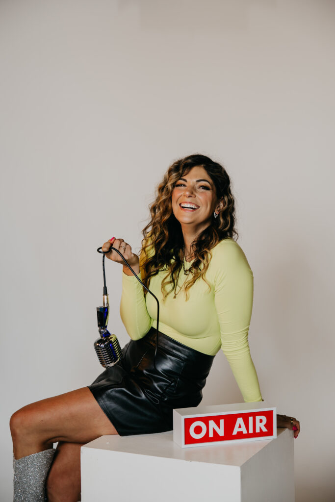 Playful image of Dr. Lauryn lying on the floor with glitter boots and microphone under an “On Air” sign during her brand photoshoot.