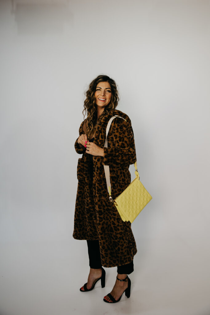 Lifestyle photo of Dr. Lauryn laughing on a red leather couch in a leopard print coat during her Minneapolis brand shoot.