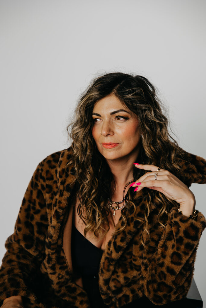 Lifestyle photo of Dr. Lauryn laughing on a red leather couch in a leopard print coat during her Minneapolis brand shoot.