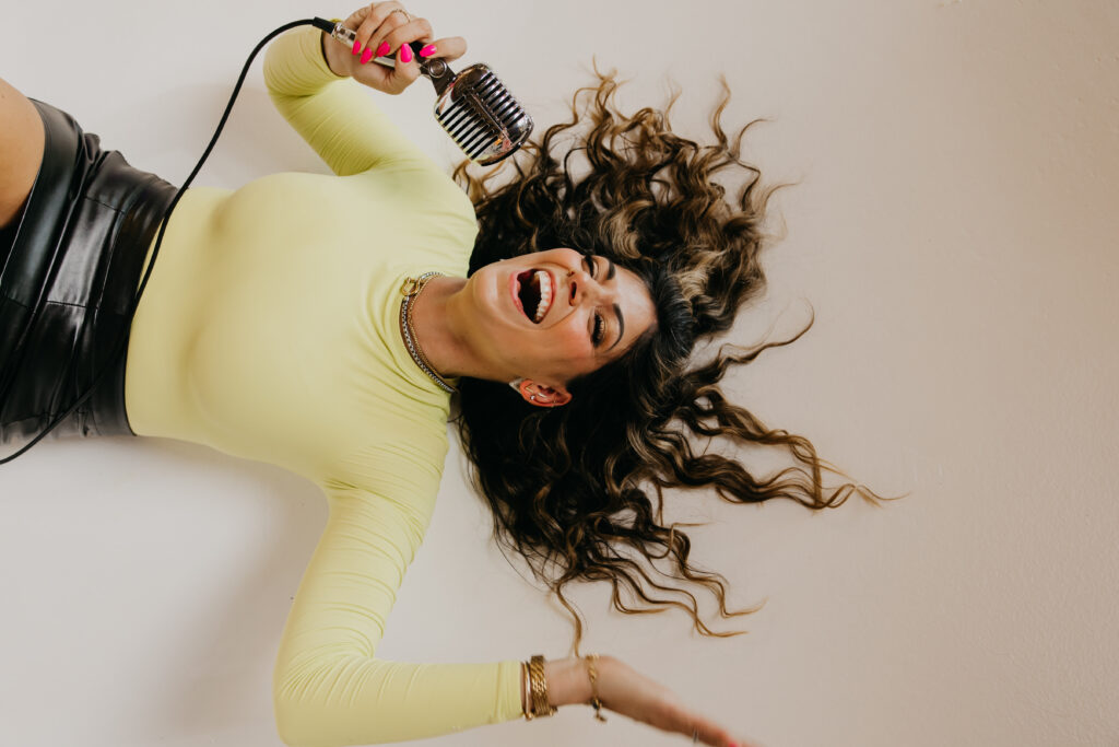 Playful image of Dr. Lauryn lying on the floor with glitter boots and microphone under an “On Air” sign during her brand photoshoot.
