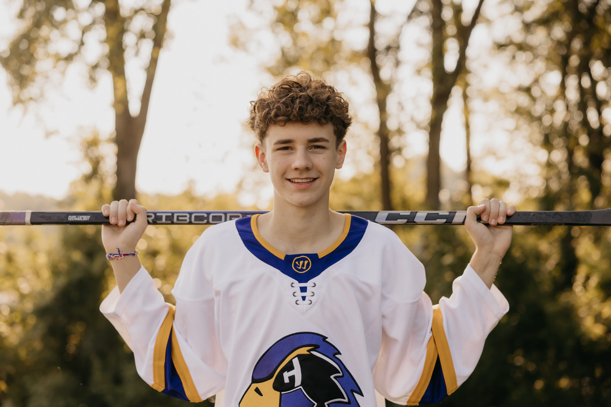 Senior boy holding a hockey stick over his shoulders during his Twin Cities senior photo session with Mycah Bain Photography.