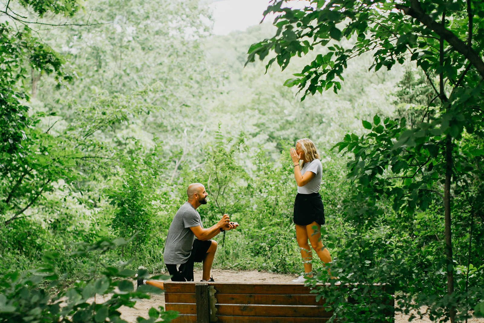 Man proposing to his partner on a forest trail surrounded by lush green trees — a romantic outdoor option for couples wondering where to propose in Minneapolis.