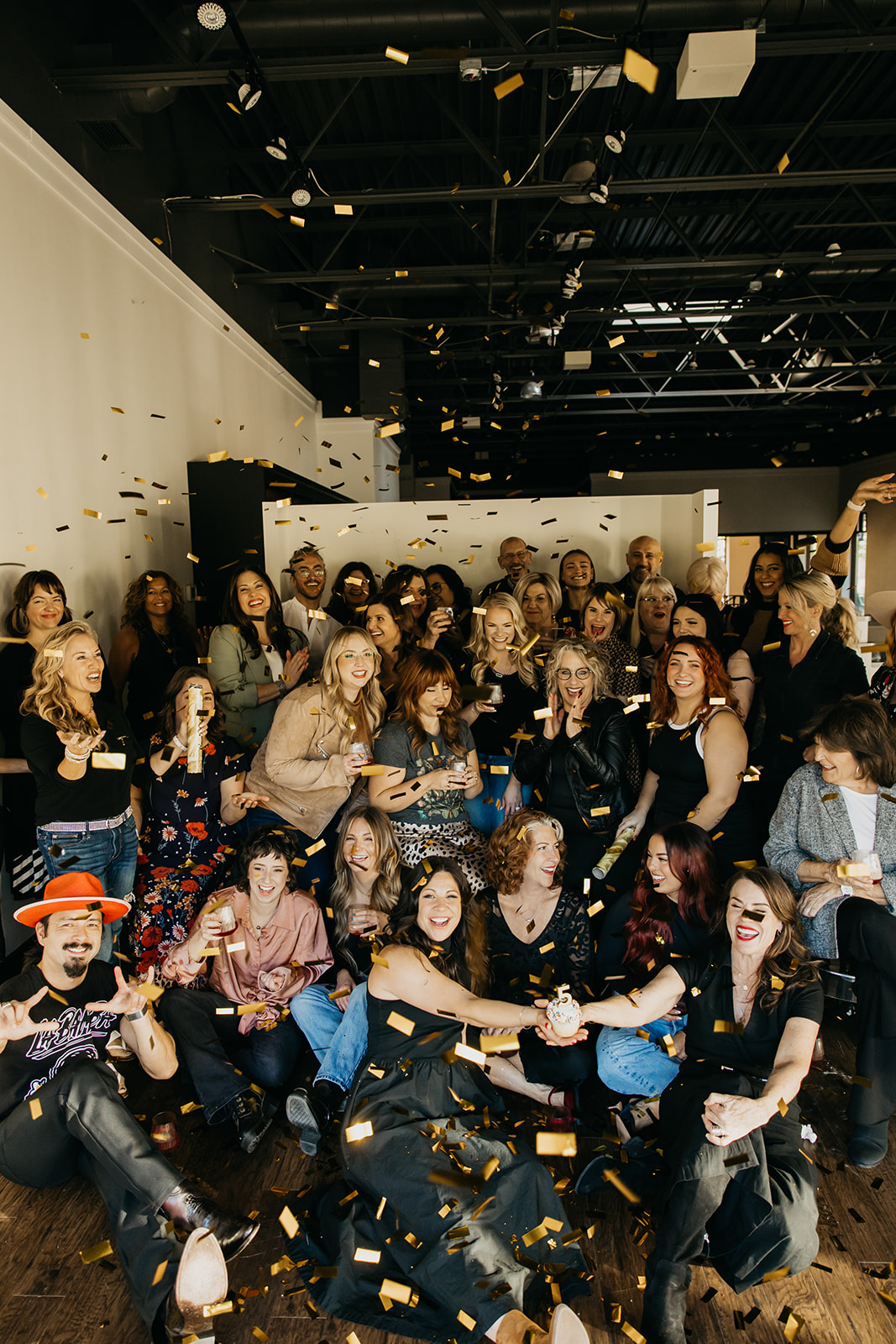 Large group of salon professionals celebrating inside District on 50th in Edina with gold confetti falling, photographed by Minnesota lifestyle photographer Mycah Bain.