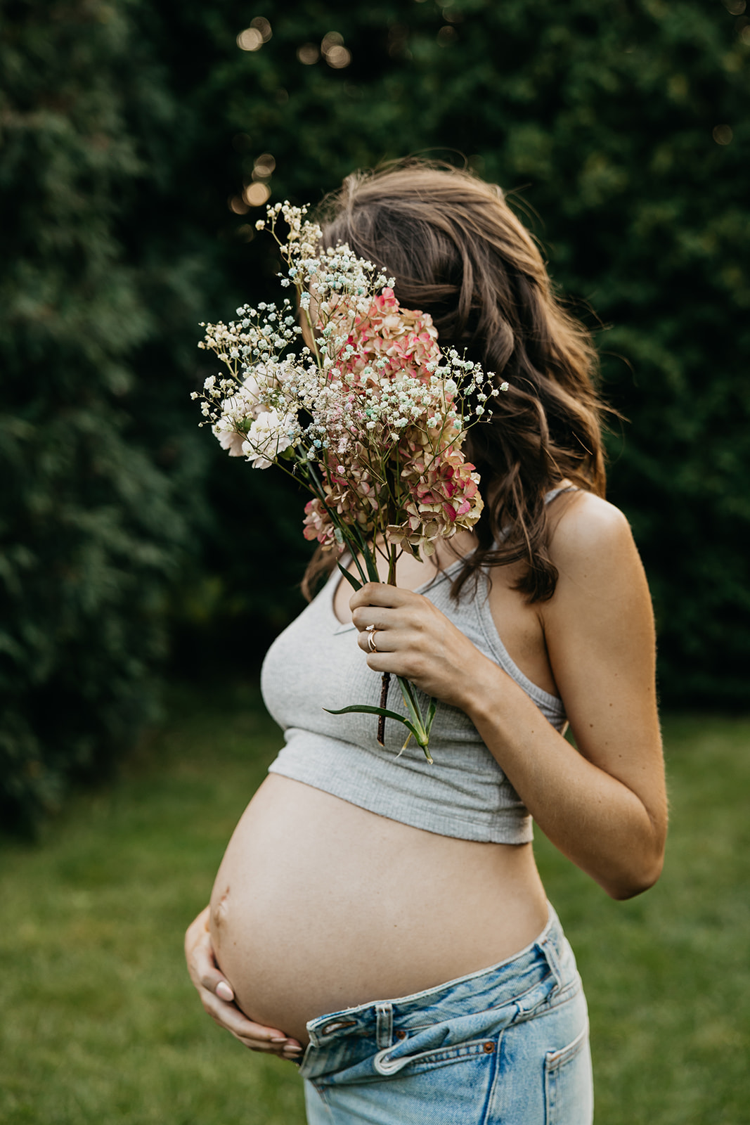 Maternity photographer in Minneapolis capturing a glowing mother-to-be holding flowers in a garden setting