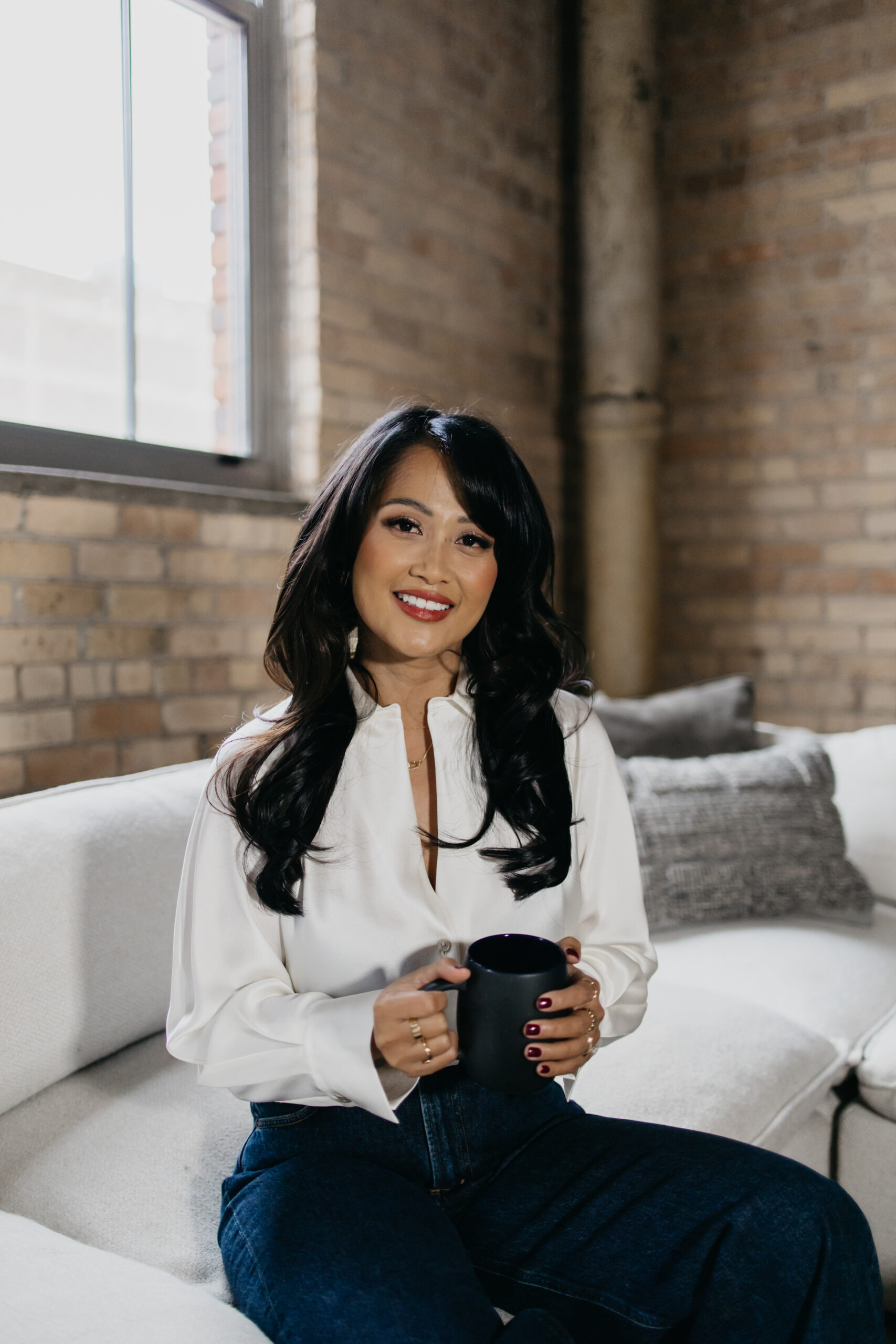 Therapist brand photos Minneapolis — Junie smiling softly in a modern brick studio, holding a mug and radiating warmth and calm confidence.