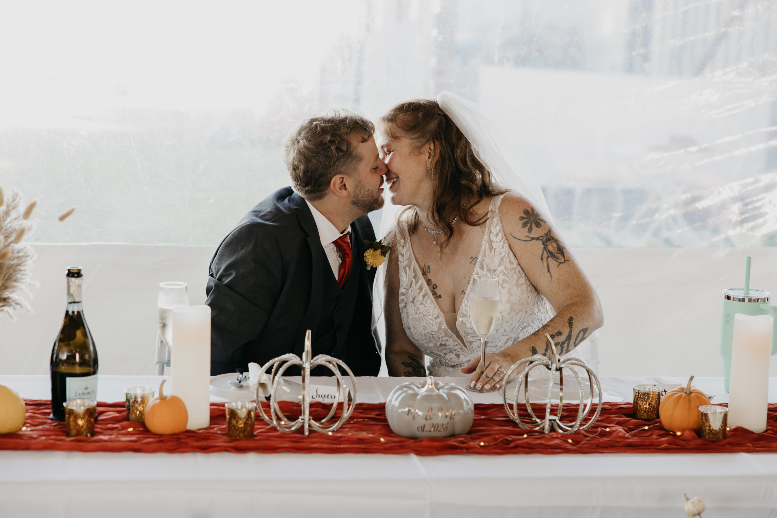 Bride and groom share a sweet kiss at their cozy fall wedding reception in Minnesota with pumpkins and candles decorating the table.