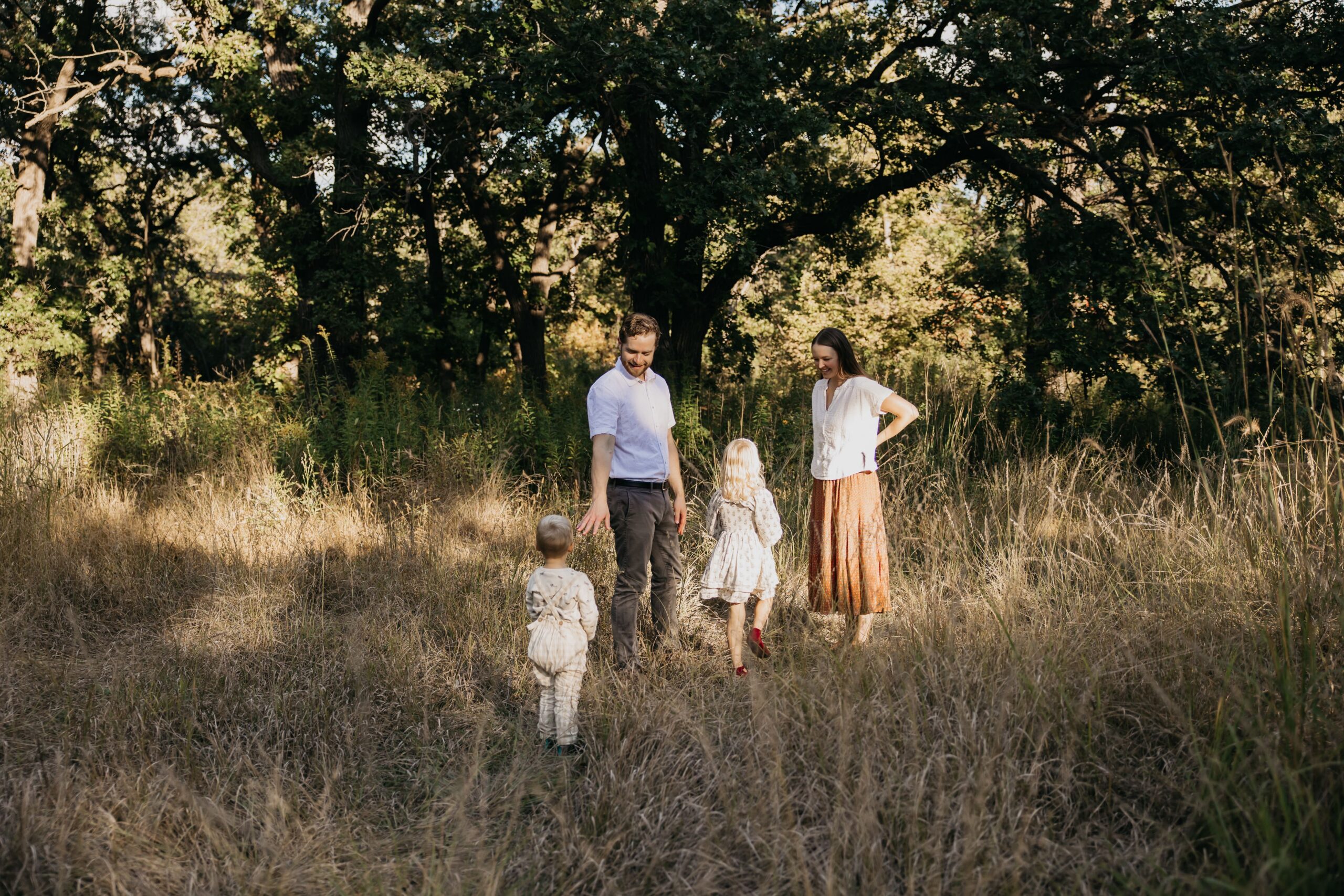 Family of four walking through a golden tall-grass field at sunset during an outdoor family photography session in Minneapolis
