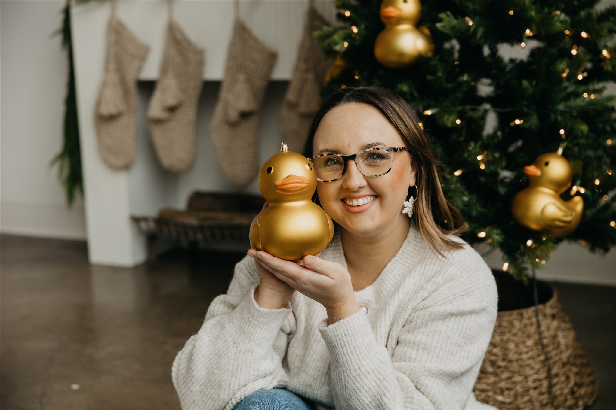 Woman holding a gold duck ornament while wearing Duck Duck Clay earrings in a cozy holiday setting