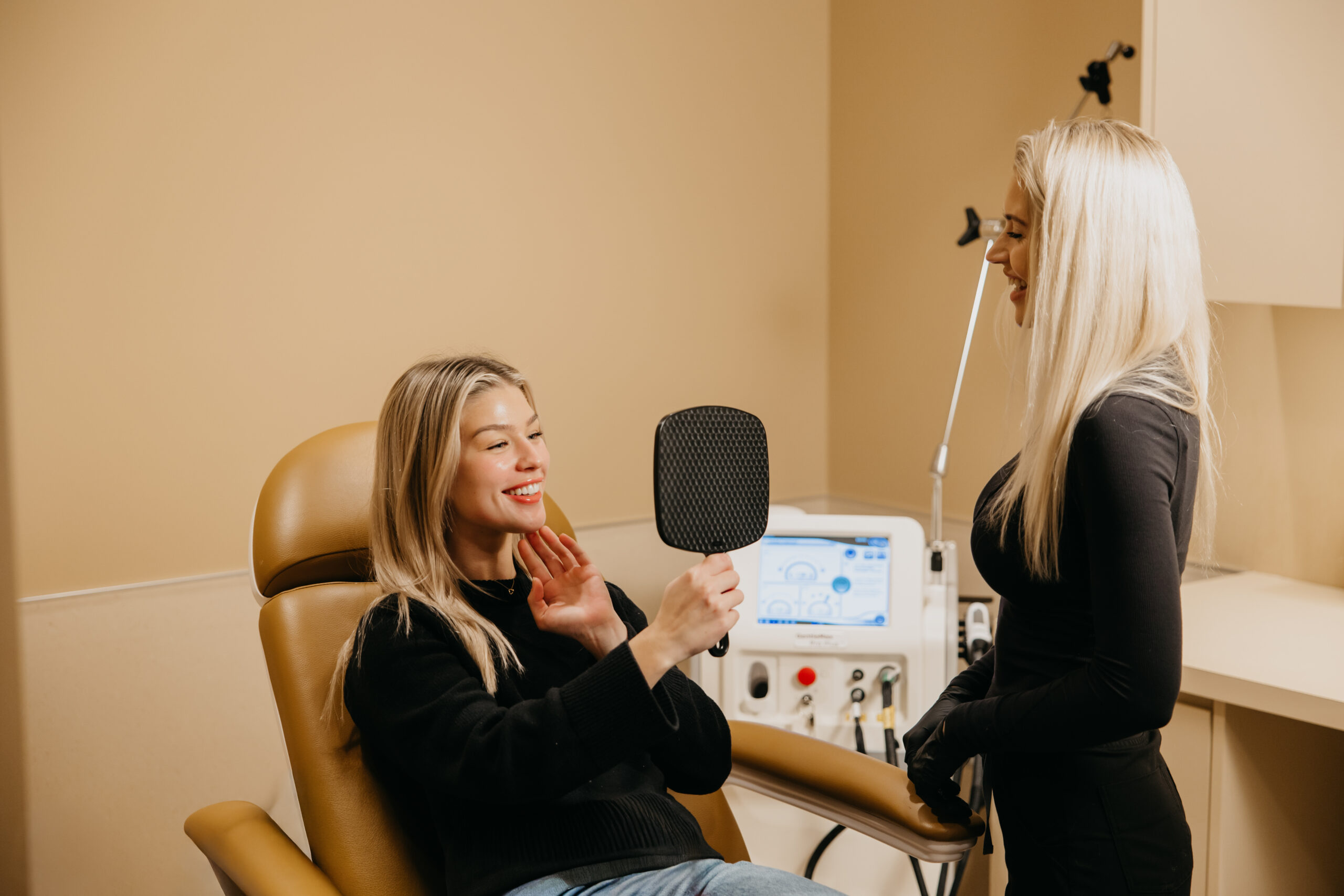 Client smiling while looking in mirror during skincare consultation at Cleo Skin Care Spa in Minneapolis, with esthetician showing treatment results