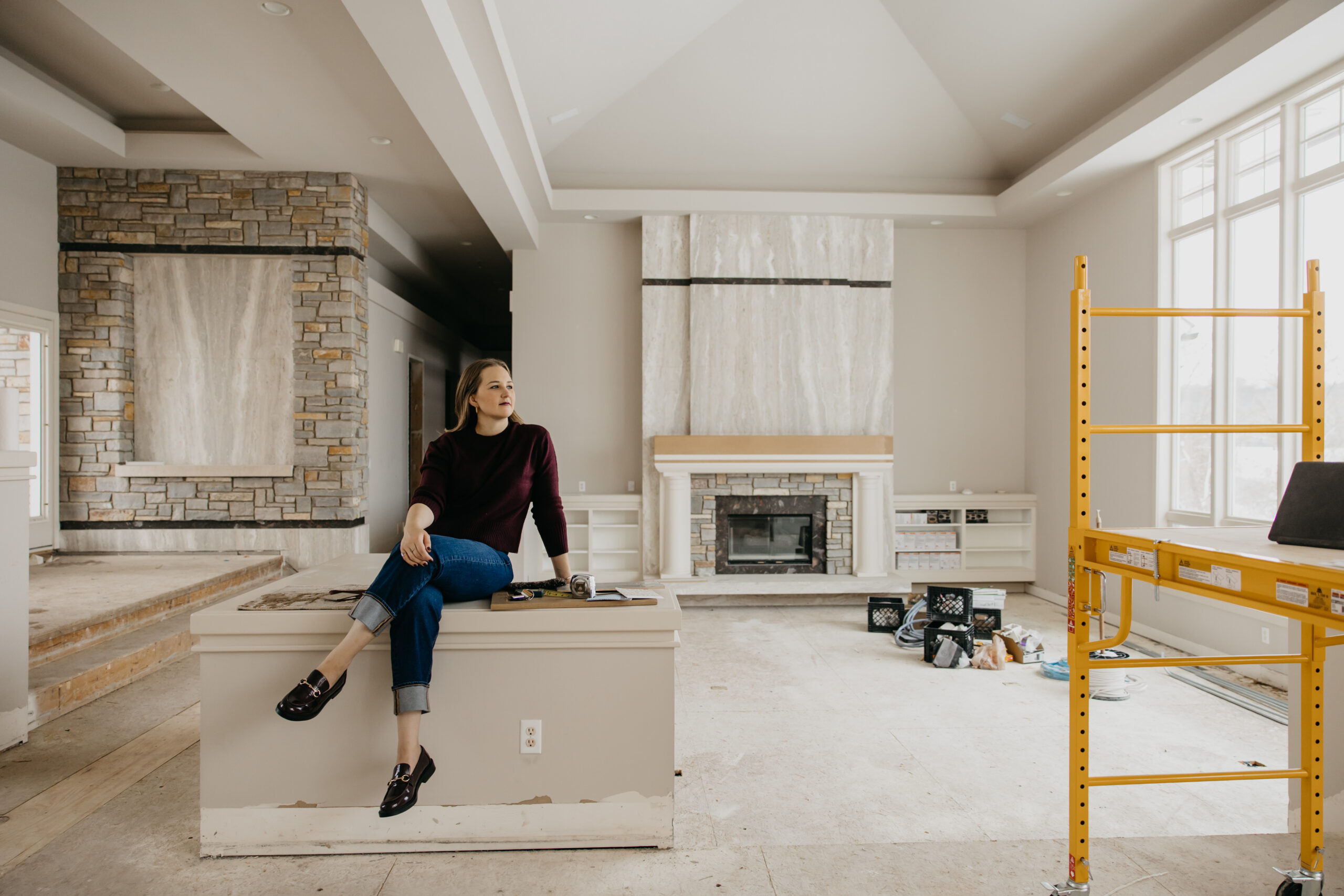 Interior designer Brittany Hanson of Hanson Haven seated on island counter in mid-construction White Bear Lake custom home remodel with two stone fireplaces — interior designer brand photography Minneapolis by Mycah Bain Photography