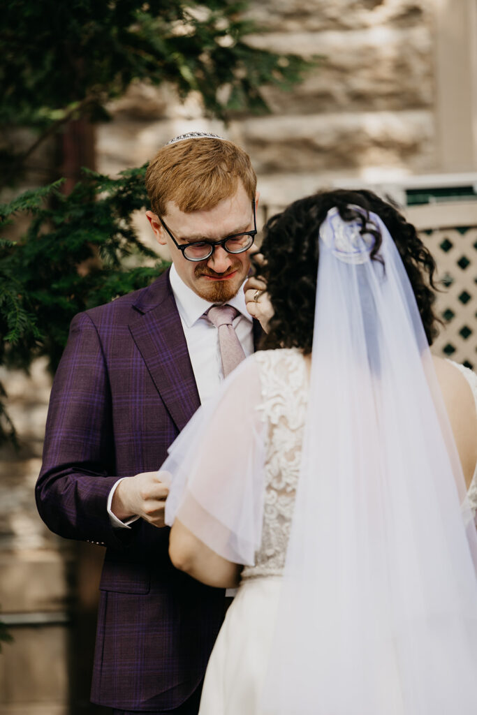 Groom reading handwritten letter to bride during emotional first look, holding her close with his arm around her lace wedding gown, documentary Jewish wedding photography by Mycah Bain Photography Minneapolis