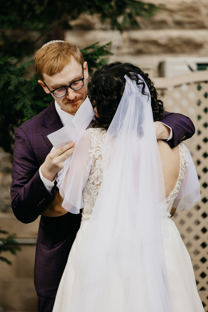 Groom in purple plaid suit laughing and crying simultaneously during emotional first look with bride at Jewish wedding in Minneapolis, documentary wedding photography by Mycah Bain Photography
