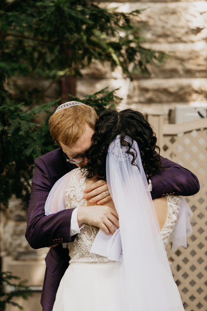Groom in purple plaid suit wearing kippah tears up during emotional first look with bride in lace wedding gown and veil, candid documentary wedding photography by Mycah Bain Photography Minneapolis
