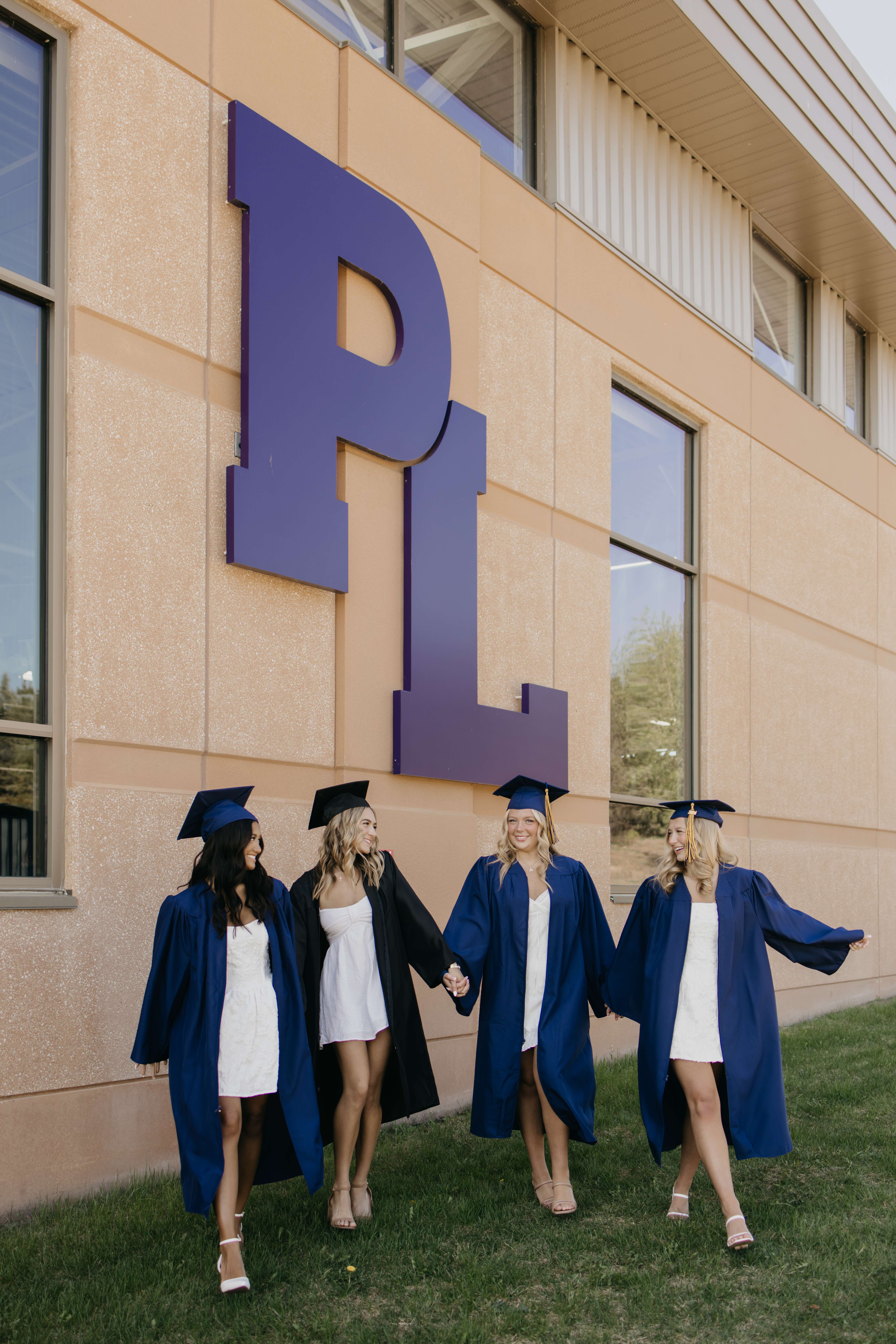 four friends in cap and gown laughing together outside their high school for graduation photos in Minneapolis