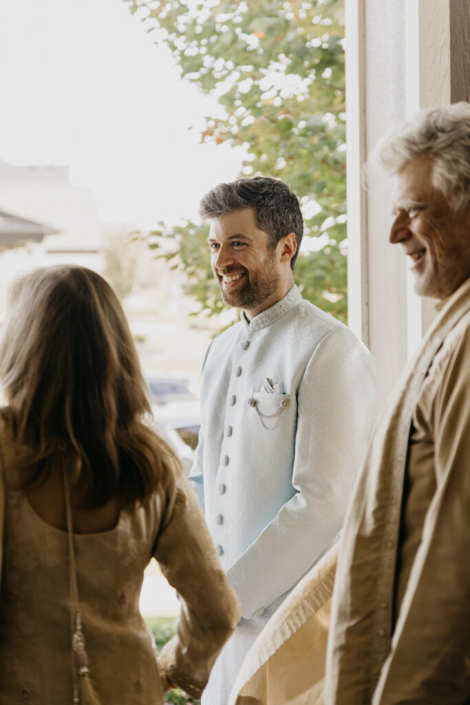 Indian groom in light blue embroidered sherwani smiling warmly at guests during pre-wedding getting ready rituals at home, South Asian wedding documentary photography by Mycah Bain Photography Minnesota