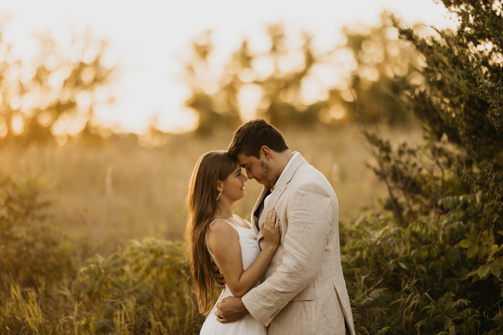 Couple nose to nose at golden hour surrounded by tall grass and warm light, sunset wedding portraits Minnesota