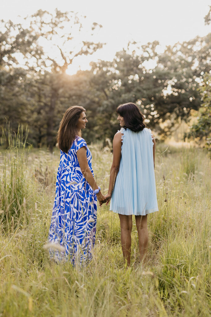 Mom and senior daughter holding hands facing each other in golden grass meadow at sunset Twin Cities senior portraits