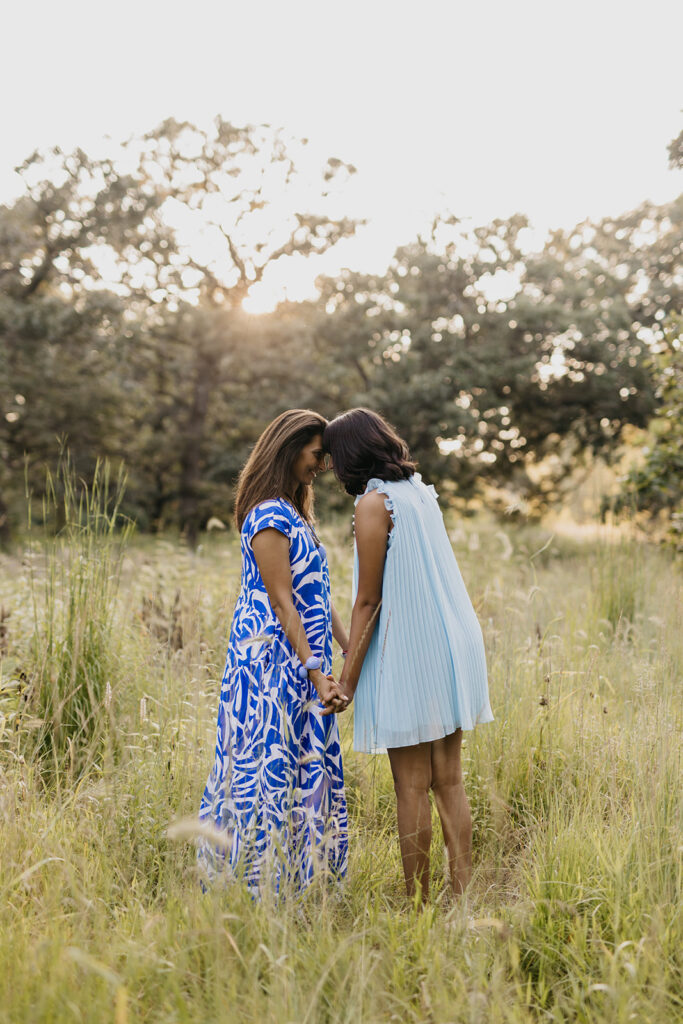 Mom and senior daughter walking hand in hand through tall grass at golden hour senior portrait session Minnesota