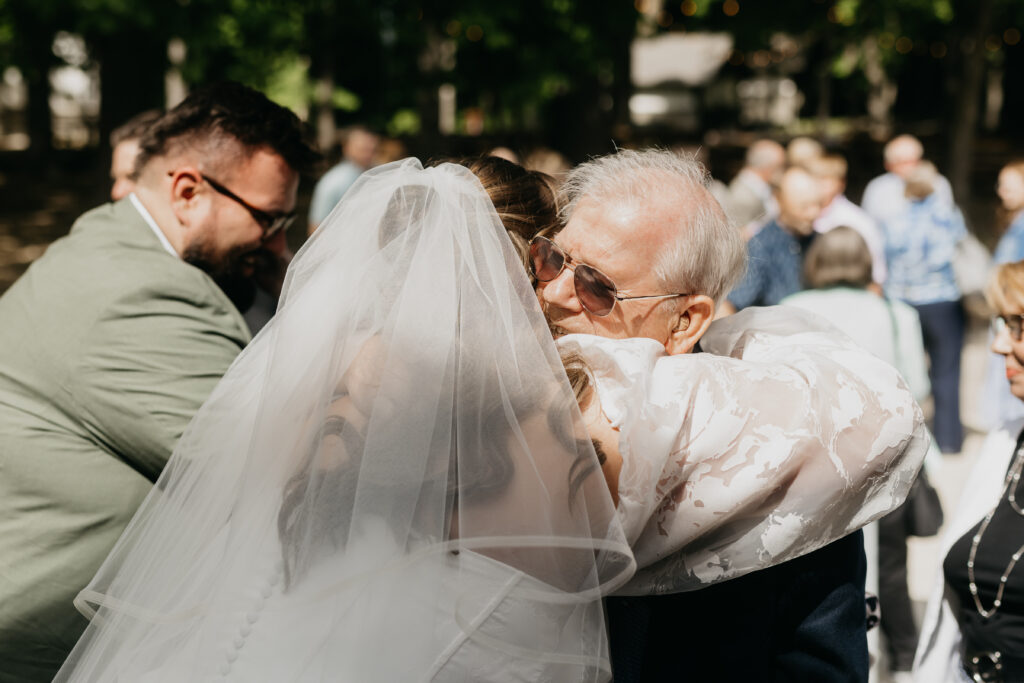 Grandfather kissing bride on the cheek under her veil after outdoor wedding ceremony in Minnesota