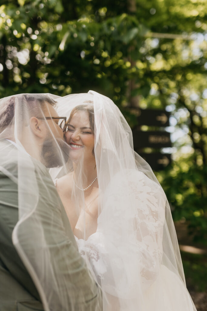 Bride and groom laughing under a veil in dappled sunlight, candid wedding photography Minnesota