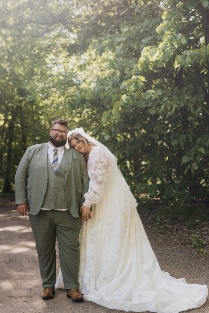 Bride leaning on groom on a shaded forest path, outdoor summer wedding portraits in Minnesota