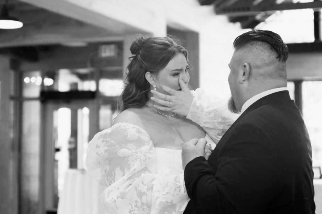 Bride crying tears of joy as groom cups her face during first look, emotional black and white wedding photography by Mycah Bain