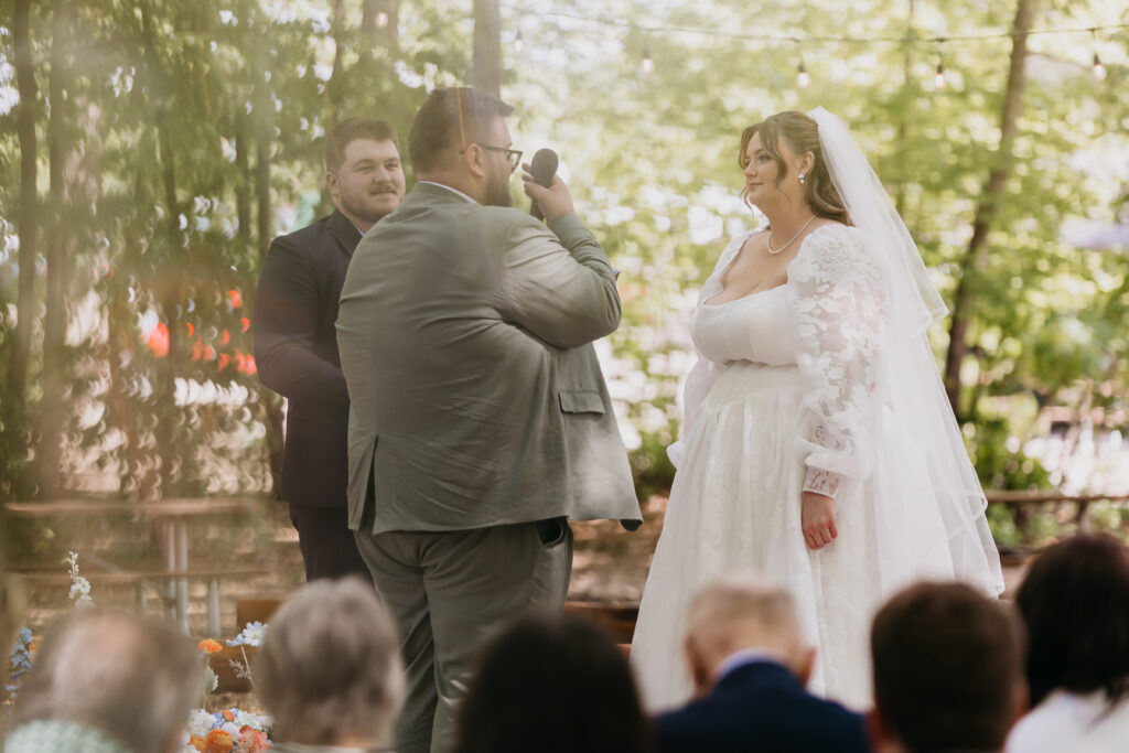Groom reading vows to bride during an outdoor woodland wedding ceremony in Minnesota