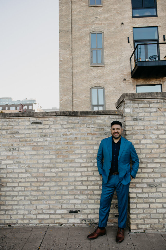 Brand photography Minneapolis — man in teal suit standing against historic brick warehouse wall in the Mill District, by Mycah Bain Photography