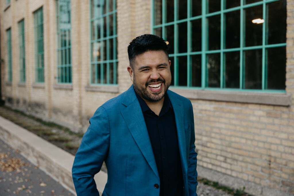Professional brand photography Minneapolis — man in teal suit laughing in front of brick building with teal windows, by Mycah Bain Photography
