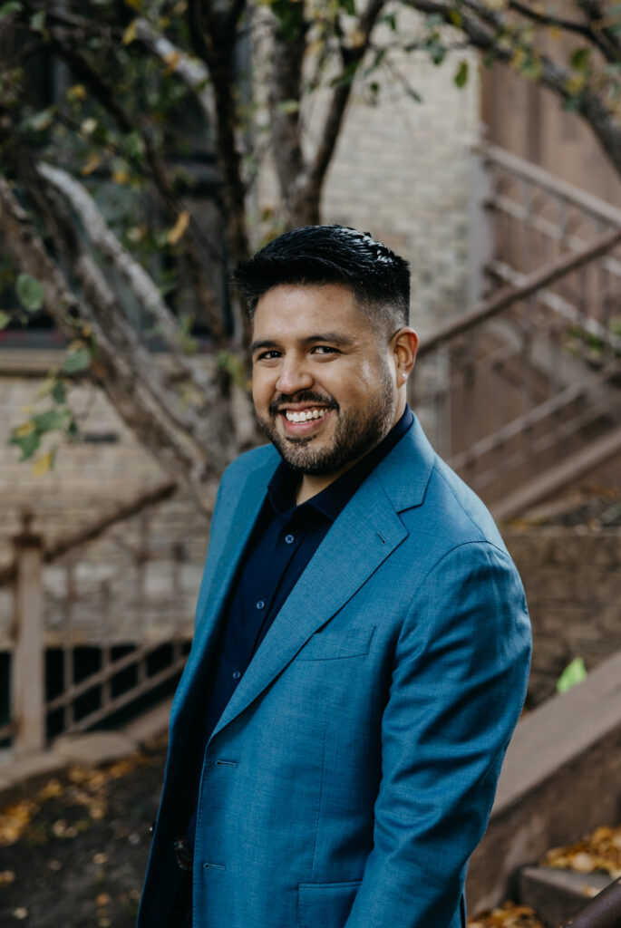 Brand portrait Minneapolis — man in teal suit smiling in profile outdoors against brick stairway and greenery, by Mycah Bain Photography