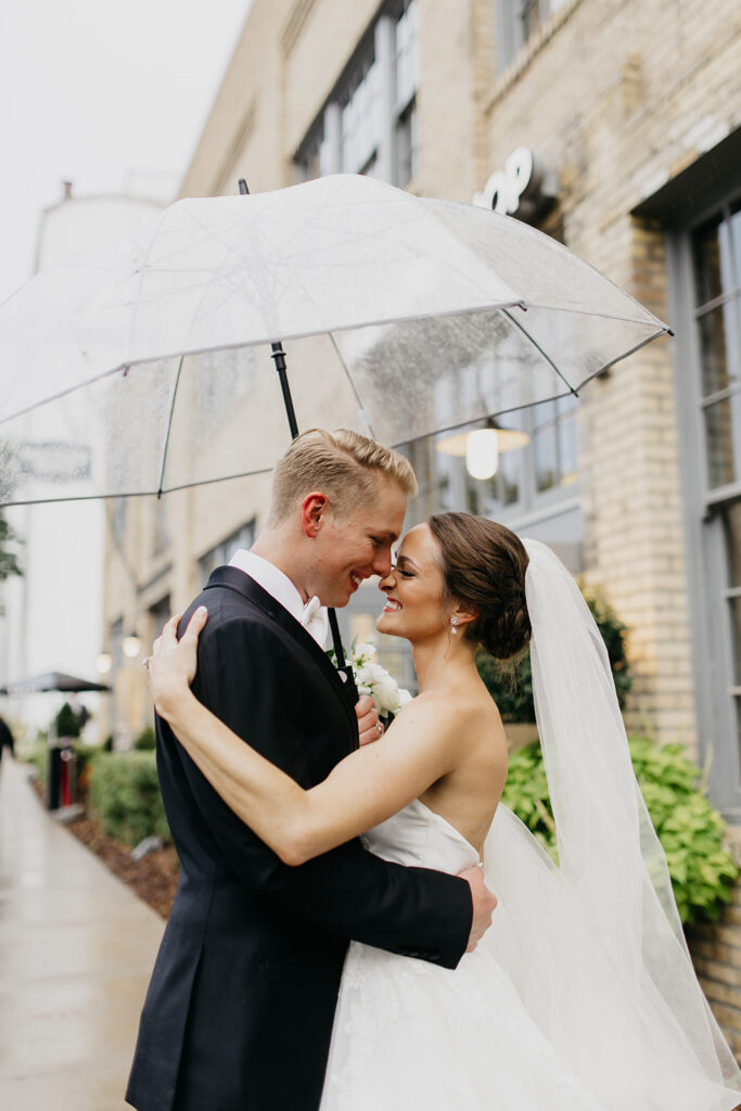Bride and groom forehead to forehead under a clear umbrella on a rainy wedding day in Minneapolis