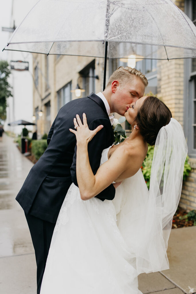 Bride and groom kissing in the rain on a wet city street with clear umbrella, Minneapolis wedding photography