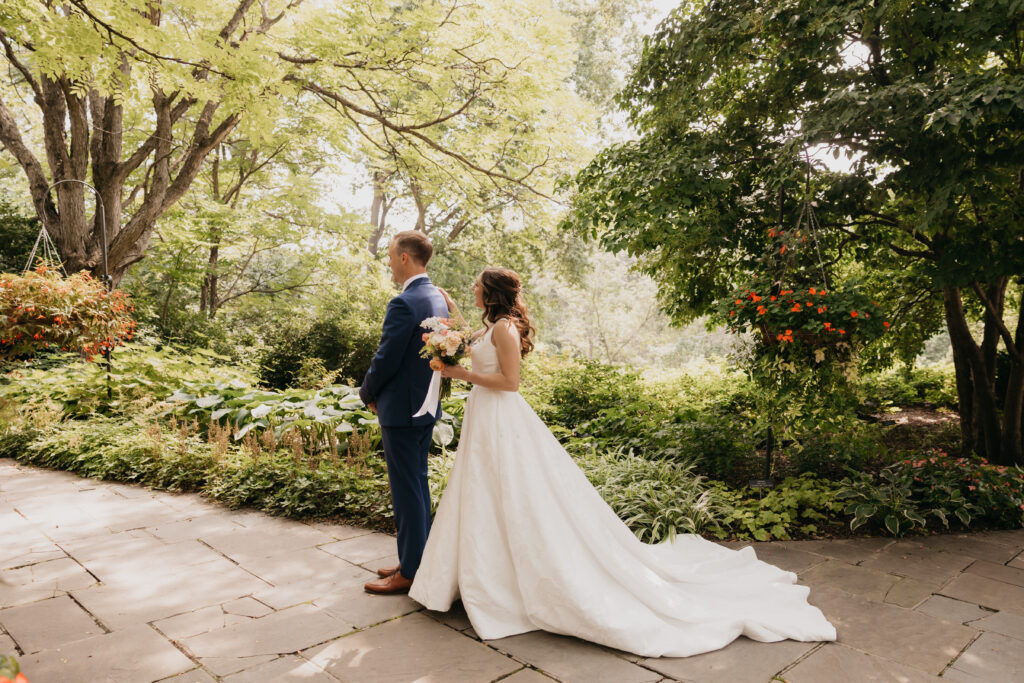 Bride and groom back-to-back first look moment in a lush garden setting, summer wedding photography by Mycah Bain Photography