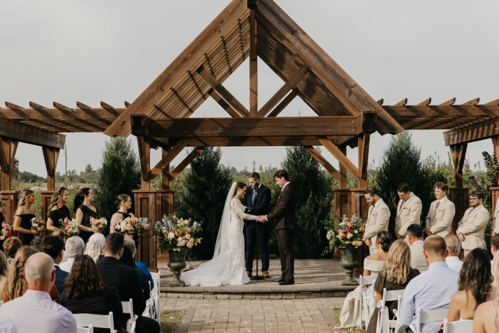 Bride and groom exchanging vows under a wooden pergola at an outdoor Minnesota wedding venue