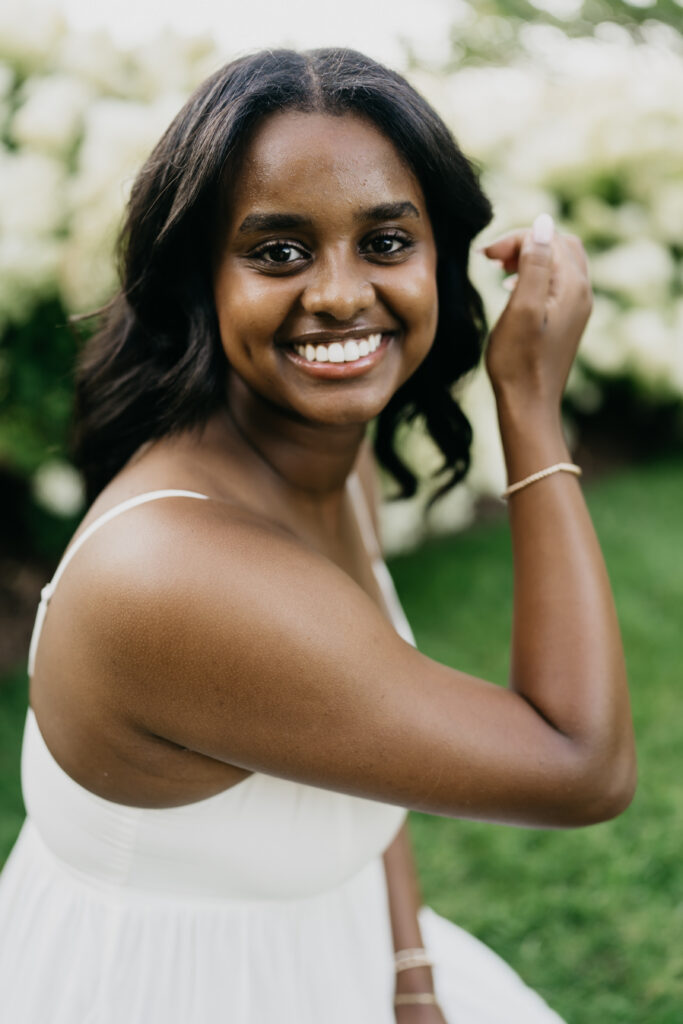 Senior girl in white tube top smiling over shoulder close up during garden senior portrait session Twin Cities Minnesota