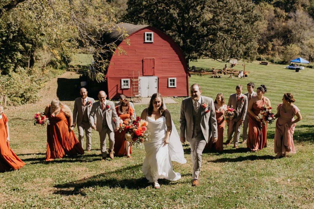 Wedding party walking across a green lawn in front of a red barn at a fall outdoor wedding in Minnesota