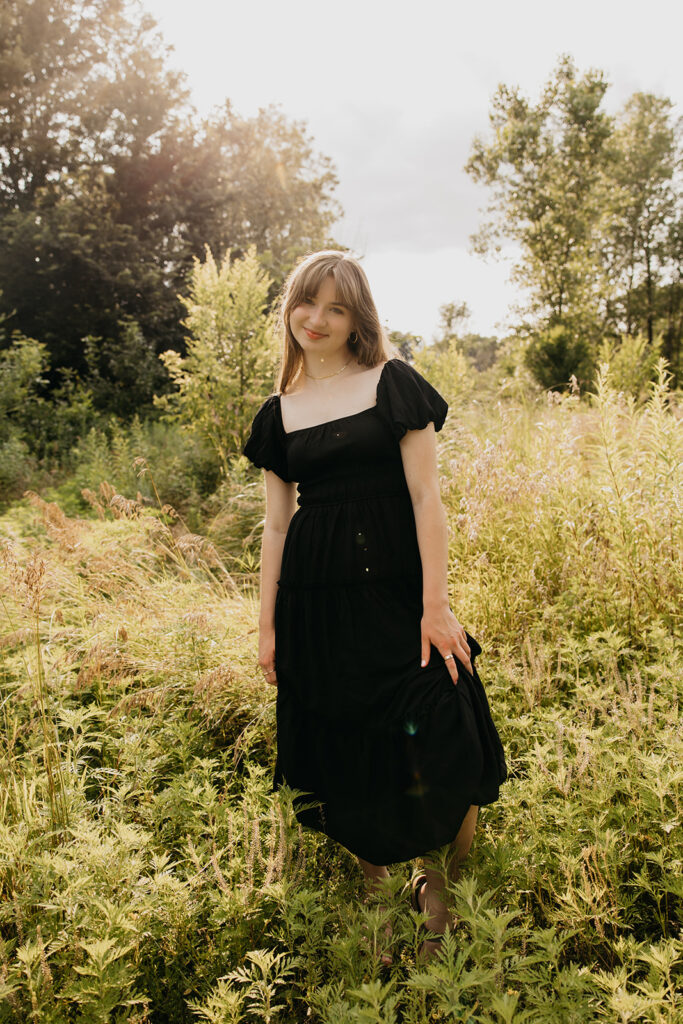 Senior girl in black dress looking directly at camera in wildflower meadow during Twin Cities senior photo session