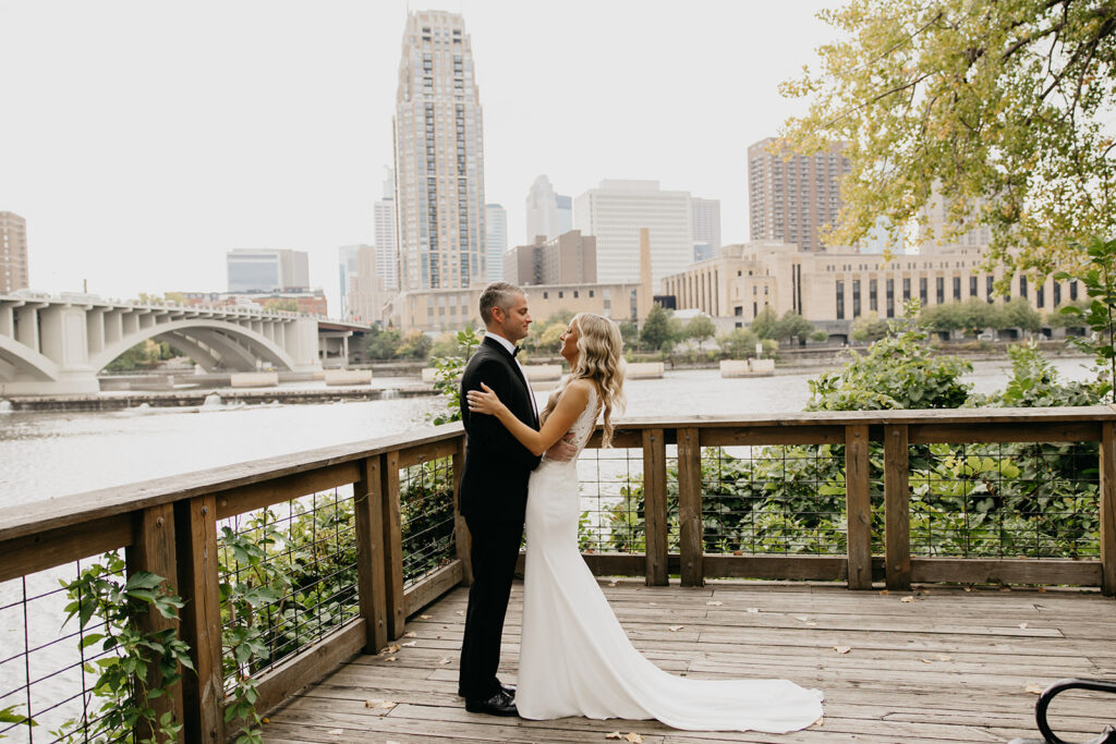 Bride and groom embracing on a riverfront deck with the Minneapolis skyline in the background